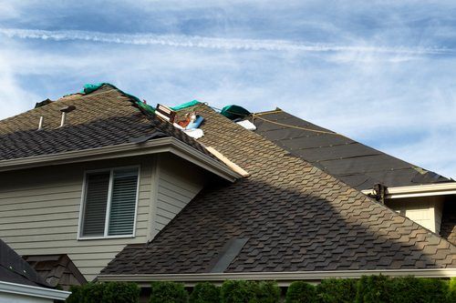 Home with roof being replaced showing new shingles, felt paper, and tools